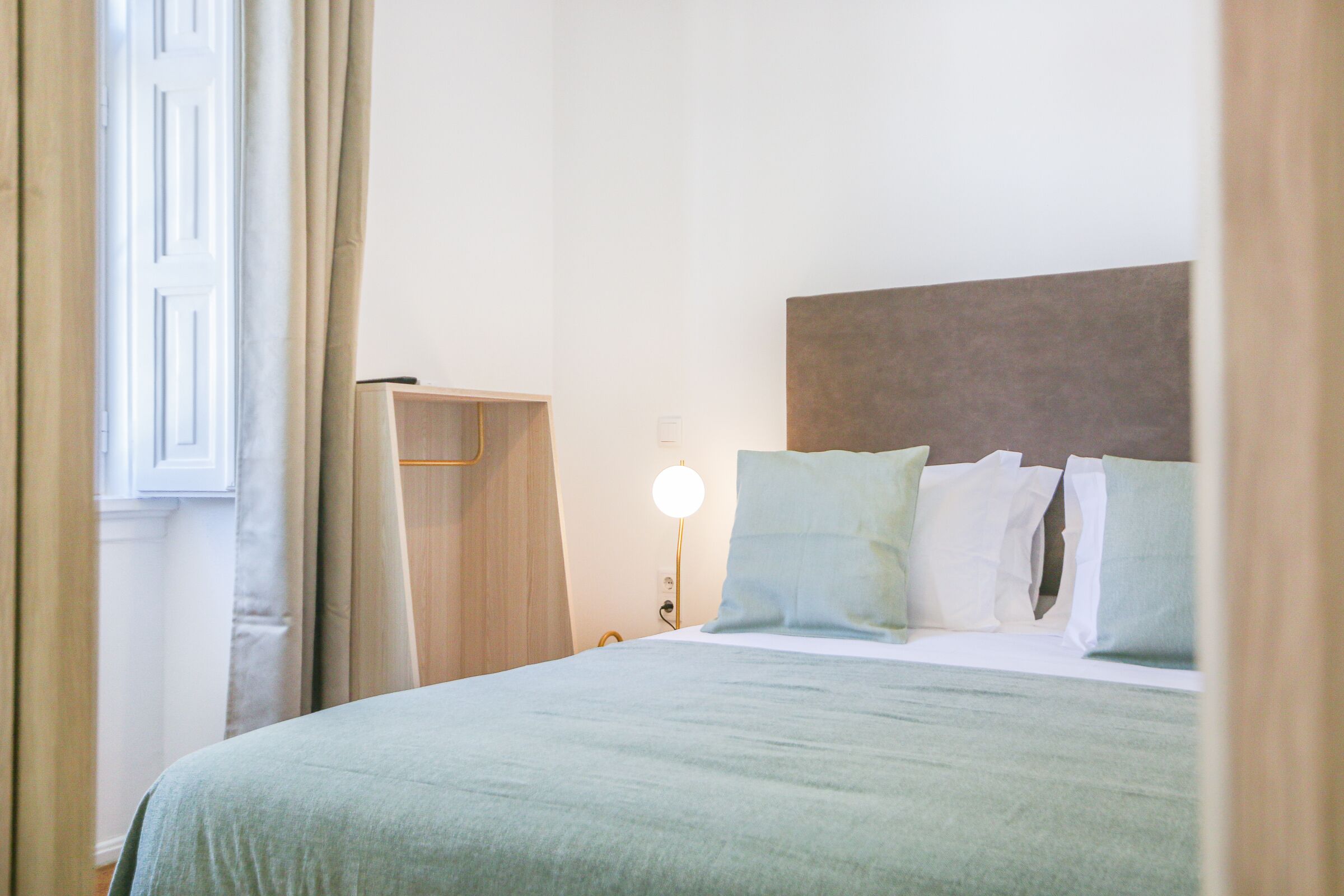 Uma cama bem arrumada com um cobre-leito verde claro, uma cabeceira de madeira e uma luminária de mesa.