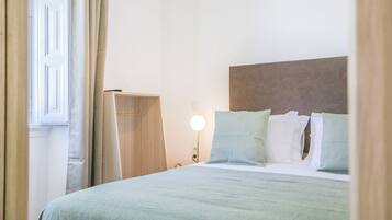 A neatly made bed with a light green bedspread, a wooden headboard, and a bedside lamp.