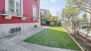 Un edificio rojo con un patio empedrado, césped verde y una valla de metal.