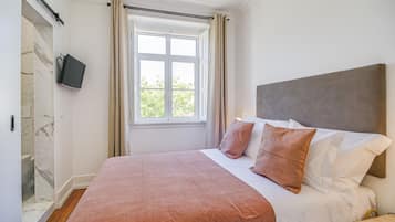 Ein Schlafzimmer mit einem großen Bett, einem an der Wand montierten Fernseher, einem Fenster mit Vorhängen und einem Duschbereich aus Marmor.