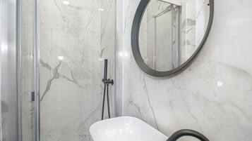 A bathroom with a glass-enclosed shower, a white sink, and a round mirror on the wall.