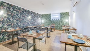 Un comedor con varias mesas y sillas, un diseño de papel tapiz floral y una ventana pequeña con plantas.