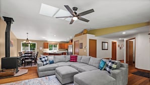 A spacious living room with a large sectional sofa, a ceiling fan, and a dining area with wooden cabinets and a chandelier. - Mt. Rainier Cabin-Hot Tub-AC-Quiet (Packwood)