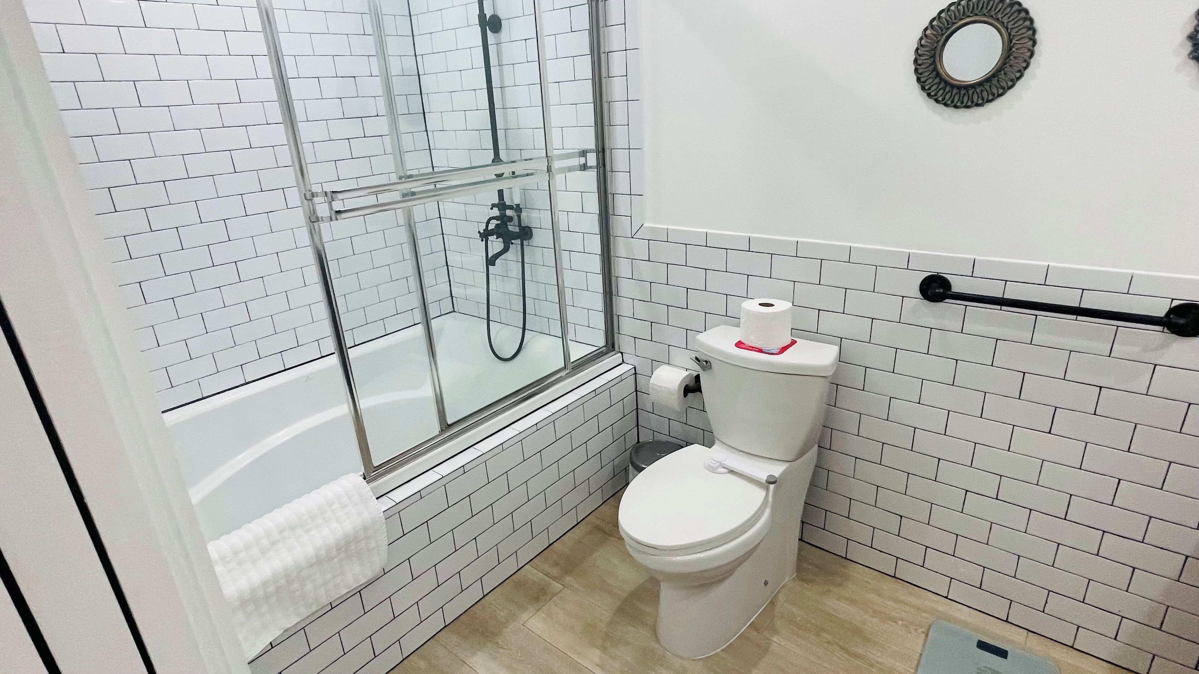 A bathroom with a white toilet, a glass shower enclosure, and a white tiled wall.