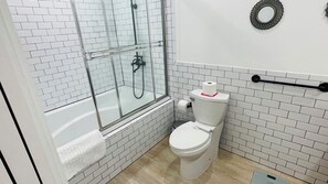 Een badkamer met een wit toilet, een douchecabine van glas en een betegelde muur.