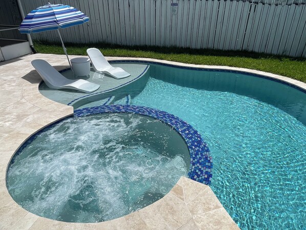 Een zwembad met een jacuzzi, ligbedden en een blauw gestreepte parasol.
