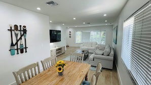 A modern living room with a wooden dining table, a sofa, and a TV mounted on the wall. - 5 Min walking to the beach Luxury pool and Jacuzzi (Hollywood)