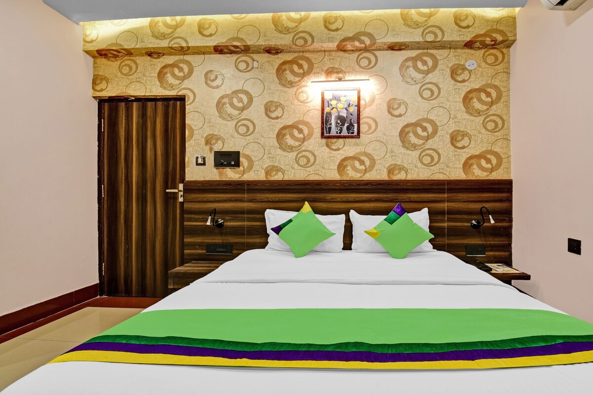 A hotel room with a bed, a wooden headboard, a wall-mounted light, and a door.