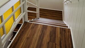 A staircase with a wooden floor and white railings, leading to a room with a window overlooking a building and plants. -  Unique getaway, 3-bedroom tropical paradise in the heart of Hilo town (Hilo)