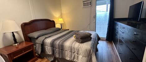 A bedroom with a wooden bed, a nightstand with a lamp, a dresser, and a television on a stand.