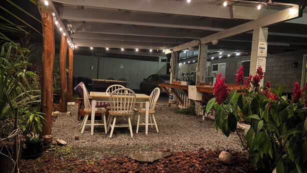 An outdoor patio area with a table and chairs, surrounded by plants and a gravel ground. -  Unique getaway, 3-bedroom tropical paradise in the heart of Hilo town (Hilo)