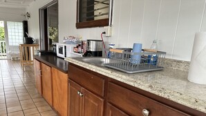 A kitchen with wooden cabinets, a granite countertop, a microwave, and a dish rack. -  Unique getaway, 3-bedroom tropical paradise in the heart of Hilo town (Hilo)