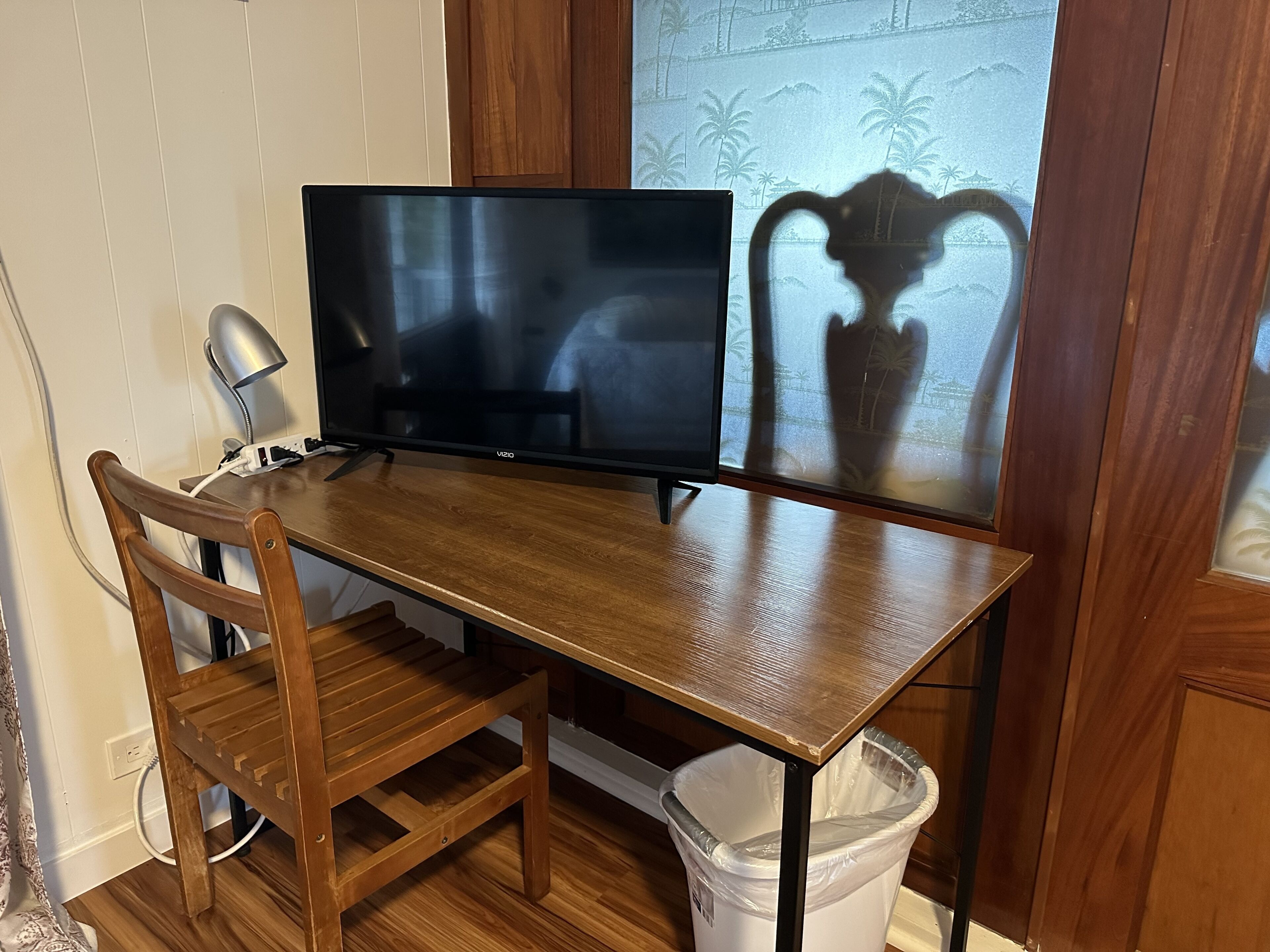 A wooden desk with a flat-screen TV, a chair, and a trash can.
