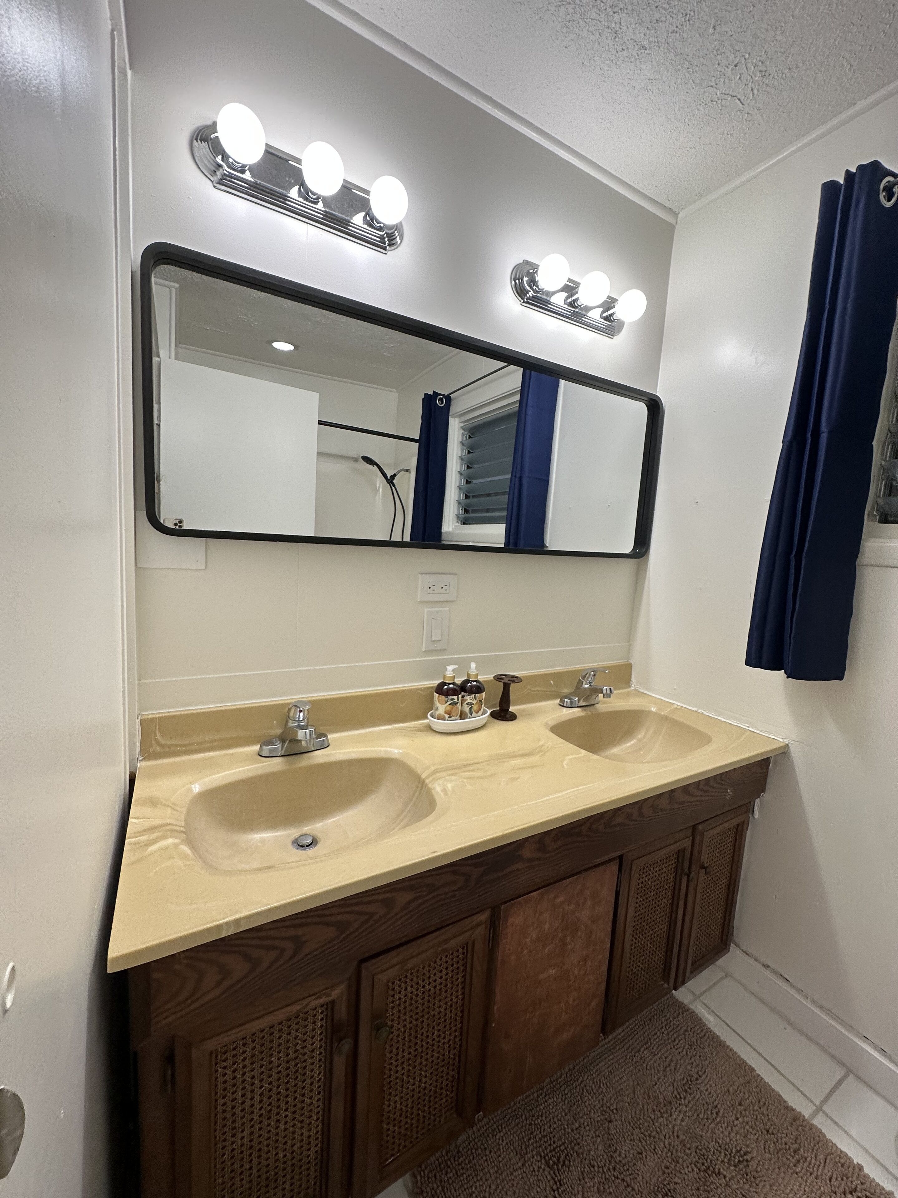 Une salle de bain avec deux lavabos, un grand miroir avec éclairage intégré et une douche visible au fond.