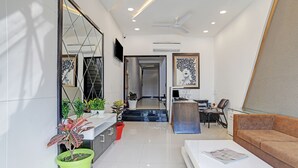 Una sala de estar moderna con un sofá, una mesa de centro y un televisor. Hay plantas en macetas y un escritorio con una silla.