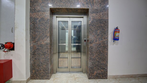 An elevator with a marble wall, a fire extinguisher, and a red object on the left. - Treebo Amaya Inn Sector 72 (Noida)