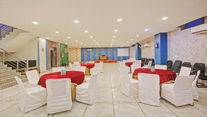 A conference room with round tables, white chairs, a stage, and a staircase. - Treebo Amaya Inn Sector 72 (Noida)