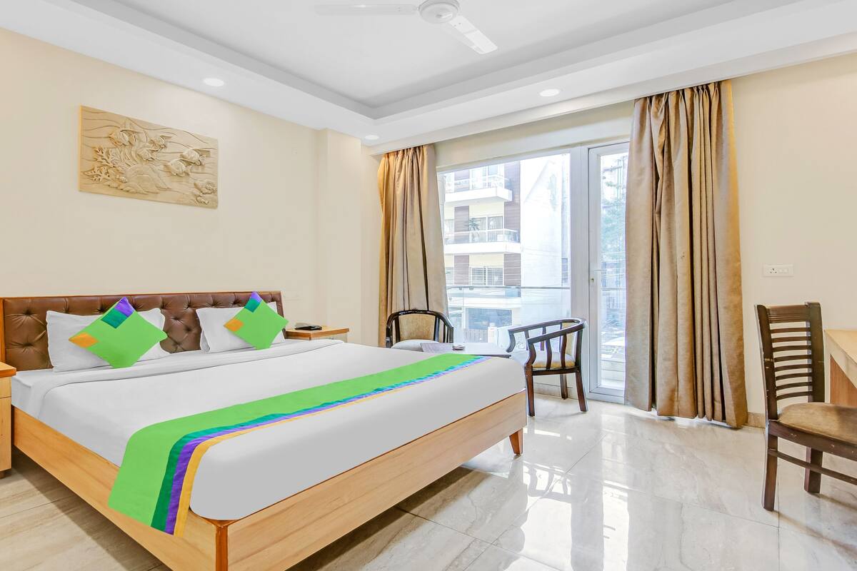 Une chambre d’hôtel avec un lit, une chaise, une table, une fenêtre avec des rideaux et un ventilateur de plafond.