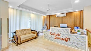 A reception area with a sofa, a desk with a laptop, and a statue. - Treebo Sai Village Gold Souk - Sec 43 (Gurugram)