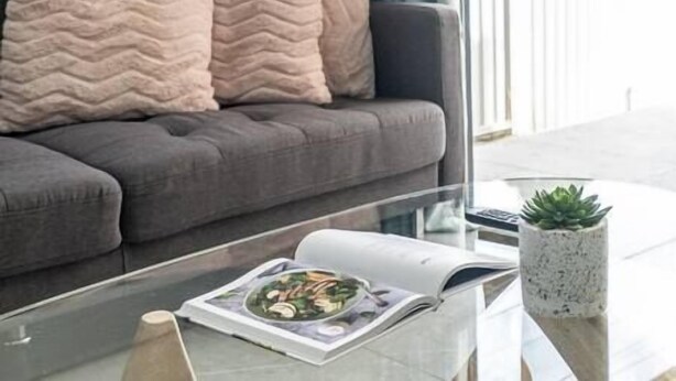 A modern living room with a grey sofa, a glass coffee table, and a magazine. - Blue Haven Retreat - Beverly Hills 208 (Beverly Hills)