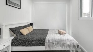 A minimalist bedroom with a bed, bedside table, and a window. - Blue Haven Retreat - Beverly Hills 208 (Beverly Hills)