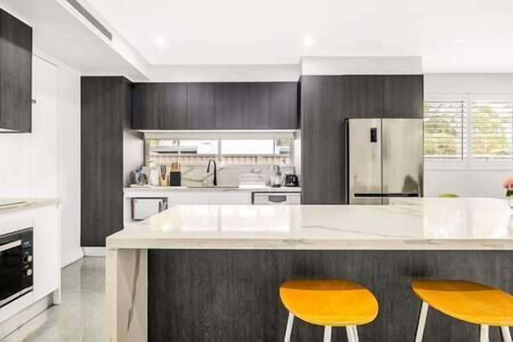 A modern kitchen with dark cabinetry, a stainless steel refrigerator, and a marble countertop.