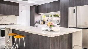 A modern kitchen with dark wood cabinetry, a large island with stools, and stainless steel appliances. - Blue Haven Retreat - Beverly Hills 208 (Beverly Hills)