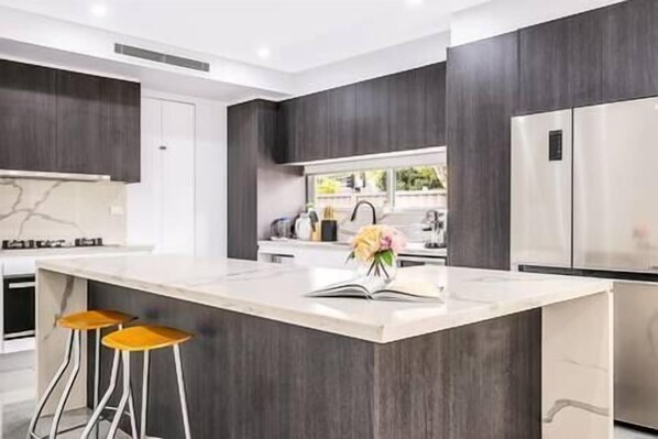 Une cuisine moderne avec des meubles de couleur bois foncé, un grand îlot central doté de tabourets et des appareils électroménagers en acier inoxydable.