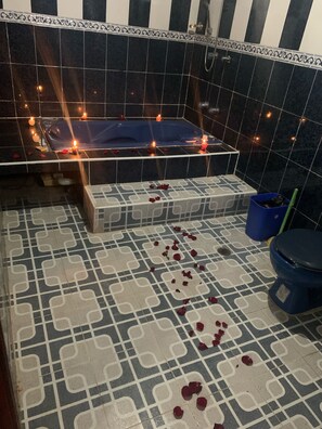 Bathroom features a bathtub and toilet, surrounded by a patterned tile floor and candles.