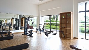 A spacious gym with various exercise equipment, large windows, and a wooden bookshelf.
