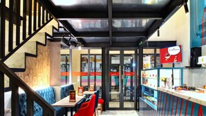 A modern restaurant with a bar area, seating with red and blue chairs, and a staircase leading to an upper level.