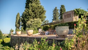 Une terrasse en pierre, agrémentée de mobilier d’extérieur et de grands jardinières, entourée de verdure et d’arbres.