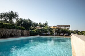A clear blue pool with lounge chairs and umbrellas, surrounded by stone walls and greenery.