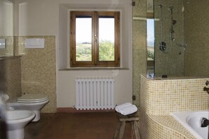 A bathroom with two toilets, a window, a radiator, and a shower area.