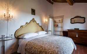 A bedroom with a large bed, a chandelier, a mirror, and a wooden dresser.