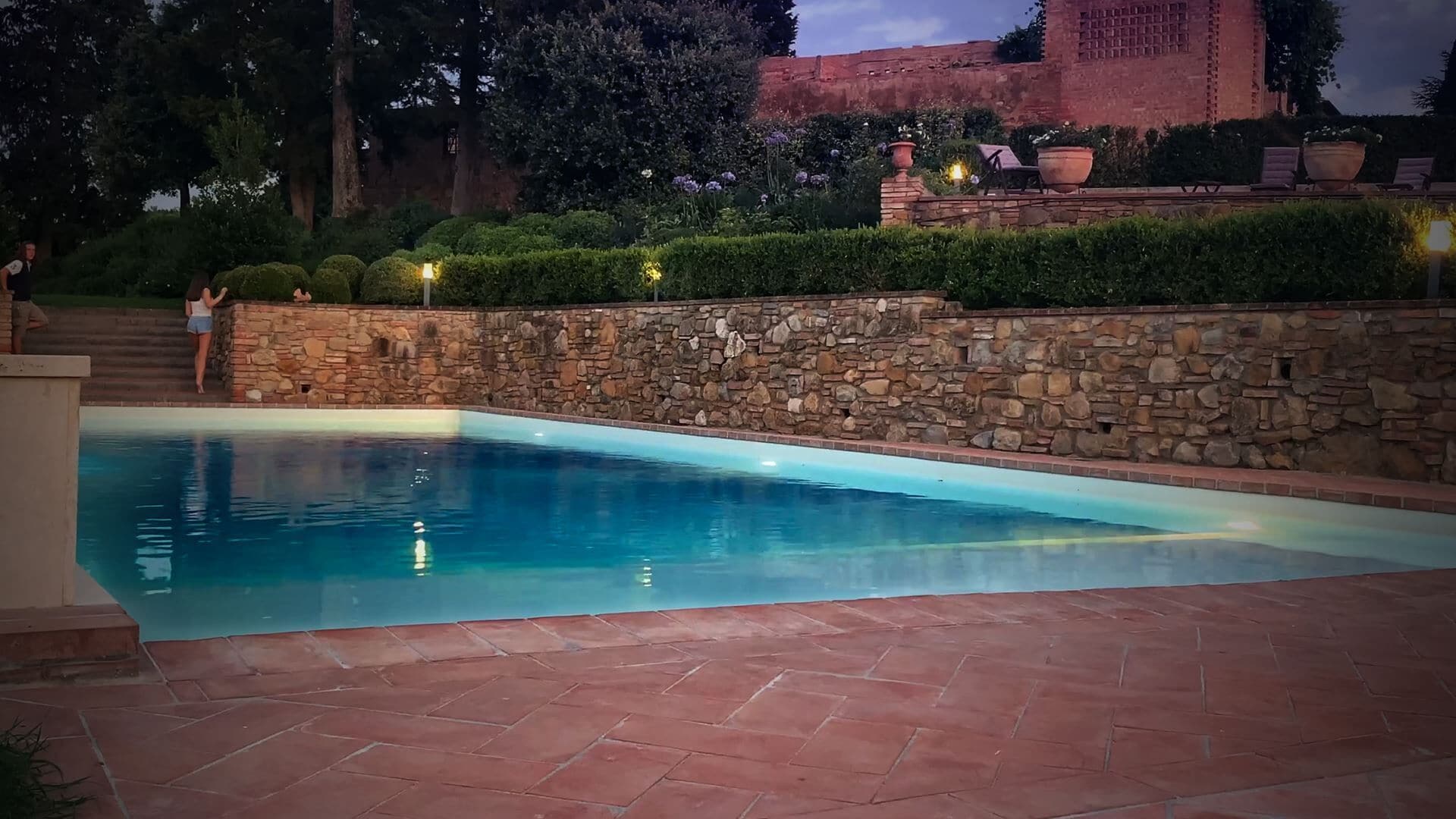 A swimming pool with stone walls and a brick patio.