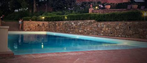 A swimming pool with stone walls and a brick patio.