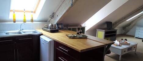 A compact kitchen with a wooden countertop, a built-in dishwasher, and a window with three bottles.
