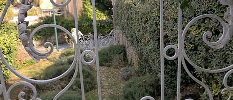 Una reja de hierro forjado con diseños intrincados, que da acceso a un jardín con setos y un camino.