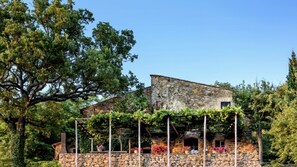 Un bâtiment en pierre doté d’un toit en pente, entouré d’une végétation luxuriante et d’arbres.