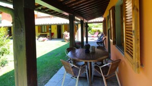 A covered patio with a round table and chairs, a yellow building in the background, and a garden area with flowers and a lawn. - Villa composed of 3 apartaments. Private pool (Castelfranco Piandisco)