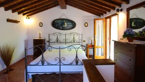 A bedroom with a bed, wooden ceiling beams, a dresser, a nightstand, and a wall-mounted lamp. - Villa composed of 3 apartaments. Private pool (Castelfranco Piandisco)