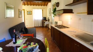 A dining area with a table set for two, a bottle of wine, and a bowl of fruit. There is a kitchen in the background with a stove and a microwave. - Villa composed of 3 apartaments. Private pool (Castelfranco Piandisco)