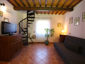 A living room with a wooden staircase, a television on a wooden cabinet, a potted plant, a sofa, and a lamp.