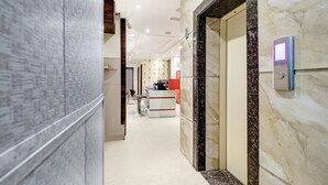 A modern hotel corridor with marble flooring, a reception desk, and a digital elevator control panel. - Itsy Hotels Unique (Amritsar)