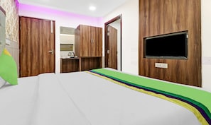 Un dormitorio con cama, armario de madera, televisor montado en la pared y una pequeña zona de kitchenette.