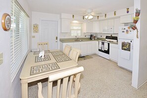 Cucina con mobili bianchi, un tavolo da pranzo con tovaglia fantasia e un frigorifero decorato con calamite.