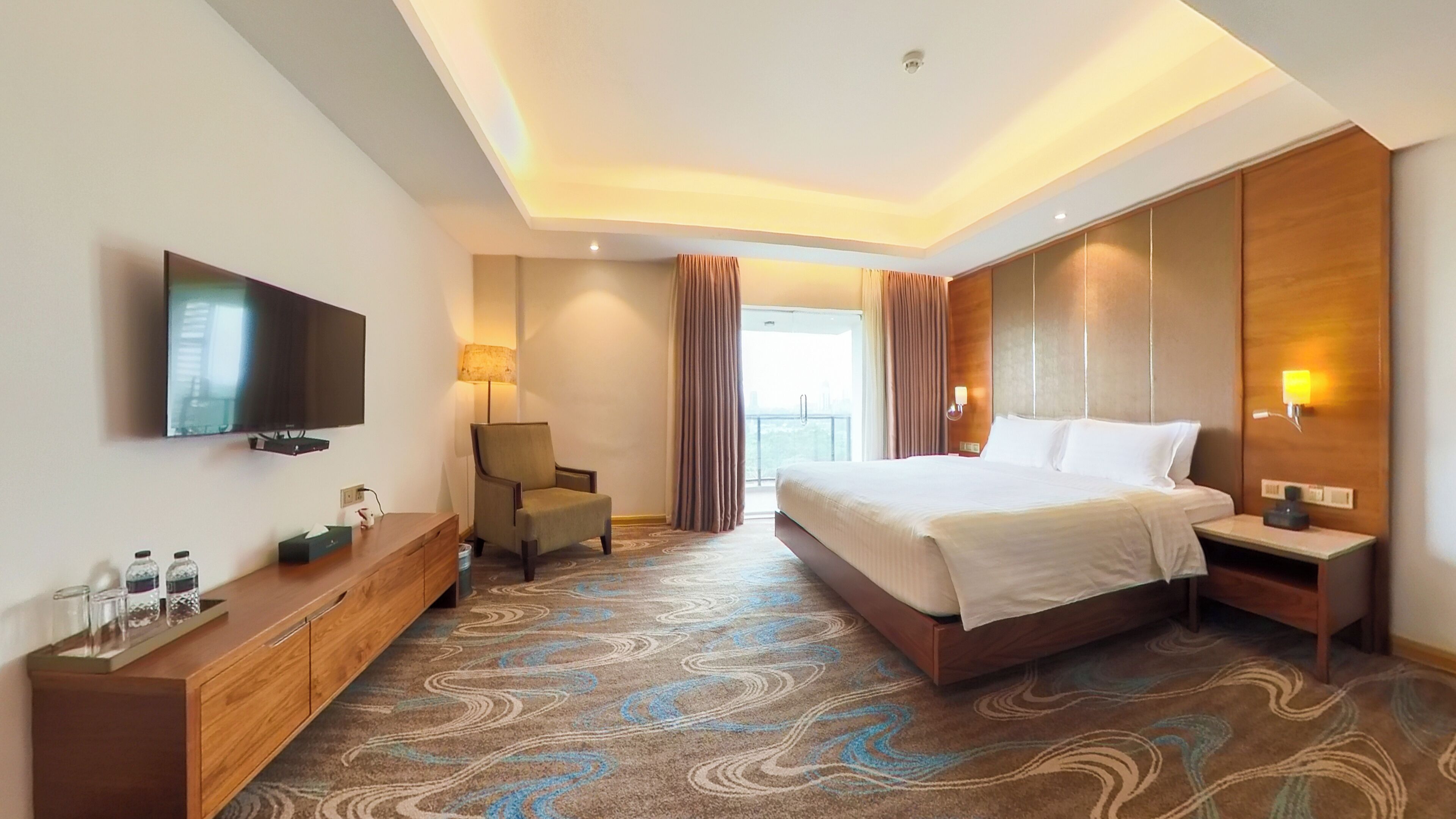 Habitación de hotel con una cama grande, televisión de pantalla plana, cómoda de madera, una silla y vistas al exterior.