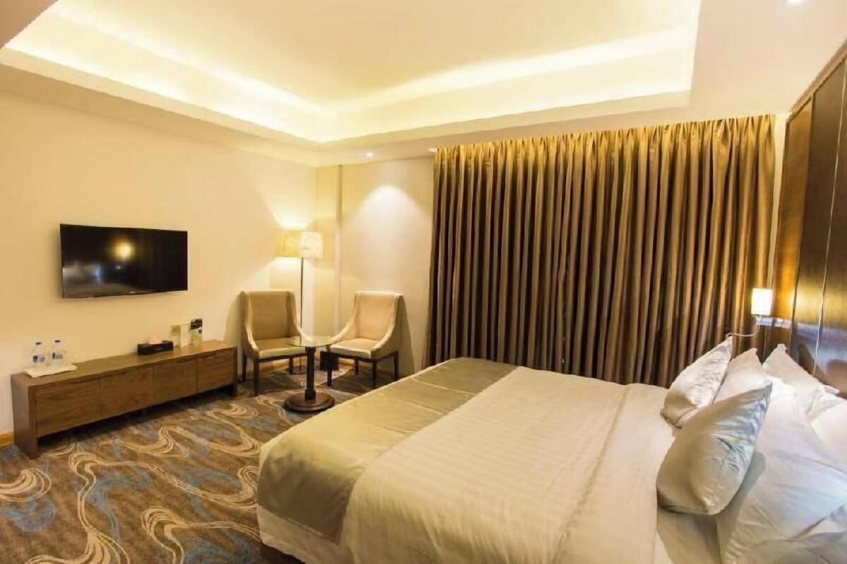 A hotel room with a bed, a TV, two chairs, a desk, and a lamp.