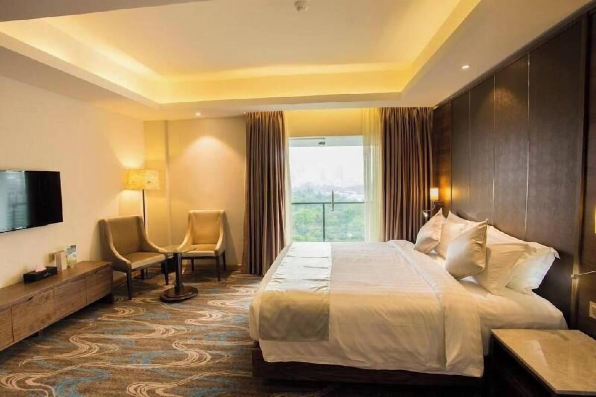 A hotel room with a bed, a TV, a desk, a chair, and a window with curtains.
